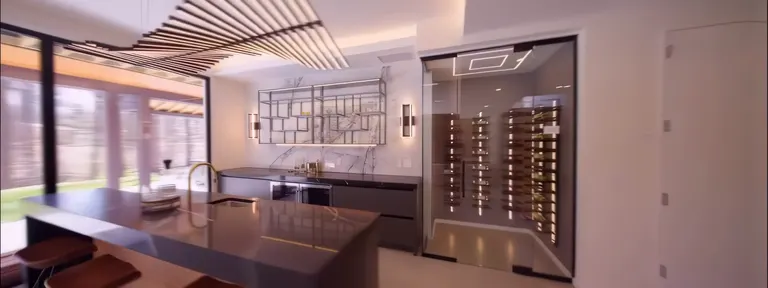 A kitchen island in dark stone beside a glazed wine room with oak racking, under a slatted wood ceiling