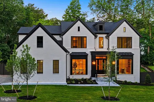 The front of the house at dusk — painted white brick under steep black-shingled gables, black-framed windows and a lit entrance