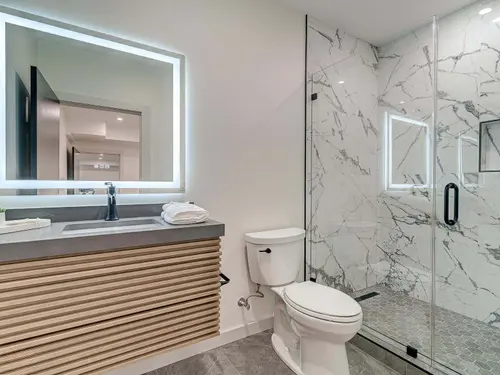 Guest bath with a fluted white oak floating vanity, backlit mirror and a full-height marble shower surround