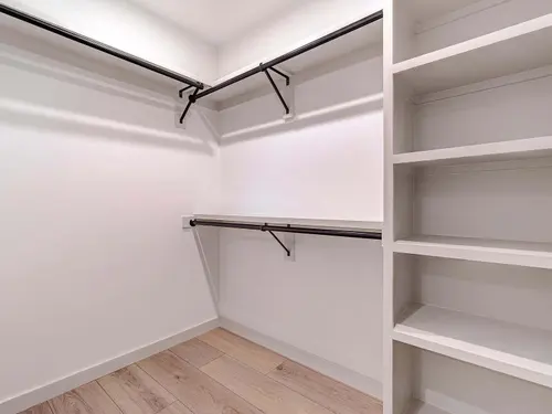 Walk-in closet built out in painted millwork — adjustable shelf bays, double-hang and long-hang rods on matte black hardware