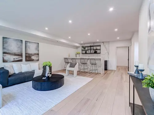 Lower-level lounge with a waterfall-edge marble bar, blackened steel open shelving and wide-plank white oak flooring