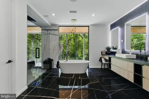 A bathroom with a freestanding tub between a glazed shower and a long oak vanity, on veined black stone