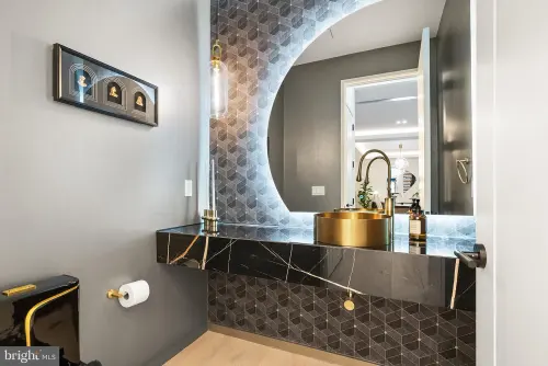 Powder room with a floating black marble vanity, hexagonal tile field and a brass vessel basin