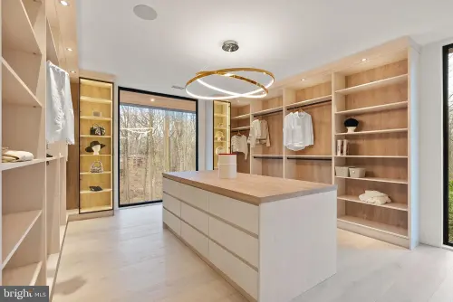 A dressing room lined with pale oak shelving and hanging rails, around an island with a wood top