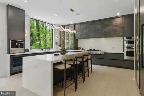 Kitchen in slab-front graphite and textured metal cabinetry with a quartz waterfall island seating four