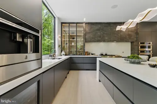 A kitchen in graphite cabinetry, with a glass-fronted display run, a stone backsplash under the hood and a marble-topped island