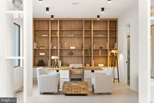 A study lined with a full-height walnut bookcase, with a built-in desk run beneath it and two armchairs facing the shelves