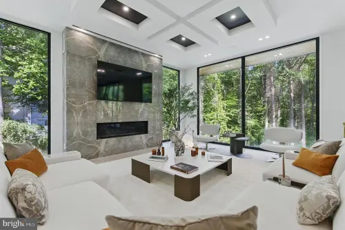 Living room with a full-height stone fireplace surround, coffered ceiling and floor-to-ceiling glazing onto the trees