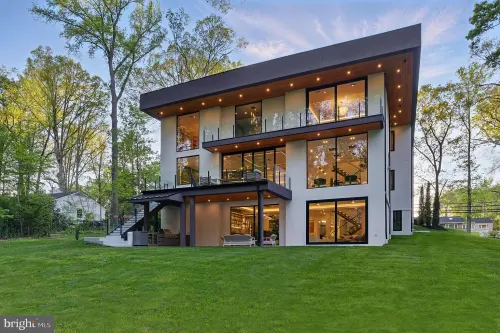 The rear elevation at dusk — three storeys of full-height glazing behind glass-railed balconies, under a deep dark fascia with a lit wood soffit