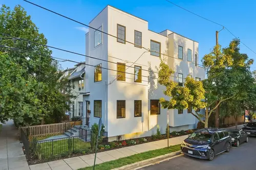 A three-story white corner house with black-framed windows on a tree-lined city street