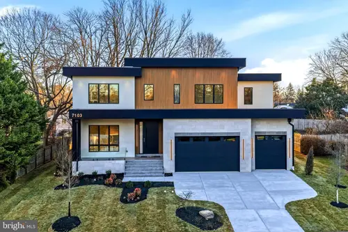 The front of the house — white stucco and pale stone around a wood-clad centre bay, black trim and a three-car garage