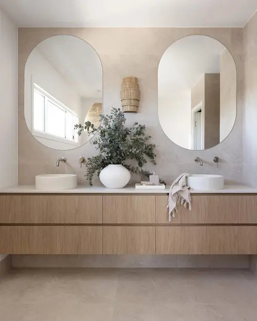 Twin oval mirrors above a wide oak vanity with two round basins and wall-mounted taps